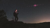 Photoillustration: Hiker using mobile device while magenta-tinted satellites orbit in the sky above