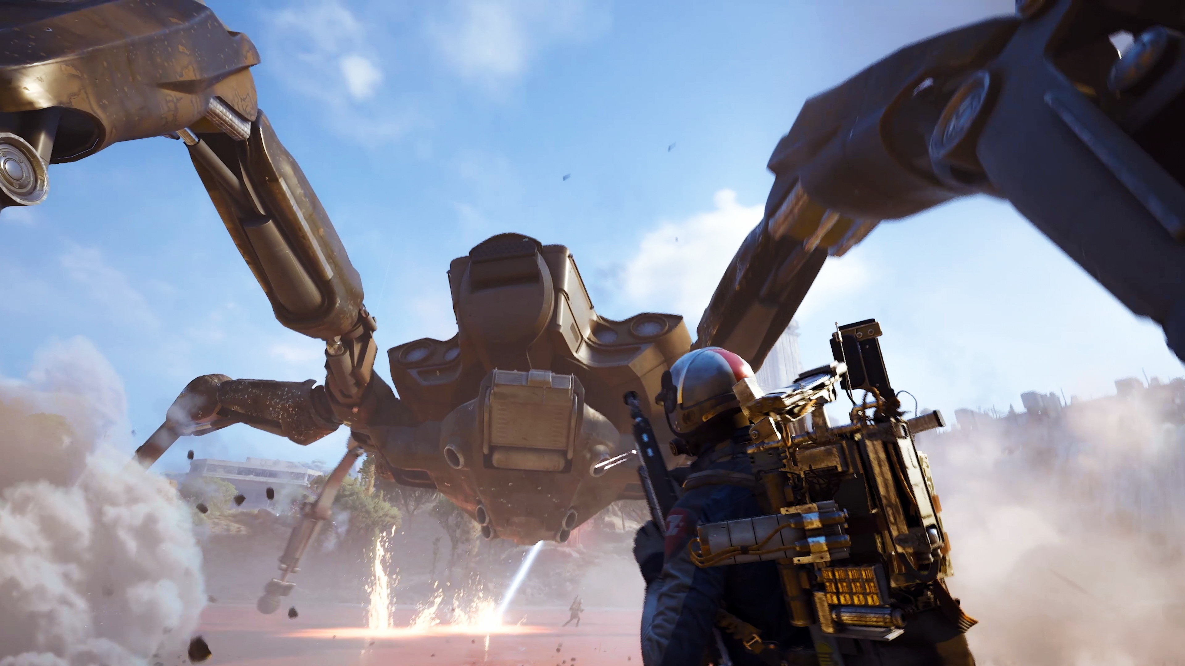 A player looking up at a massive spider-like robot as it kicks up dust and fires a laser beam.