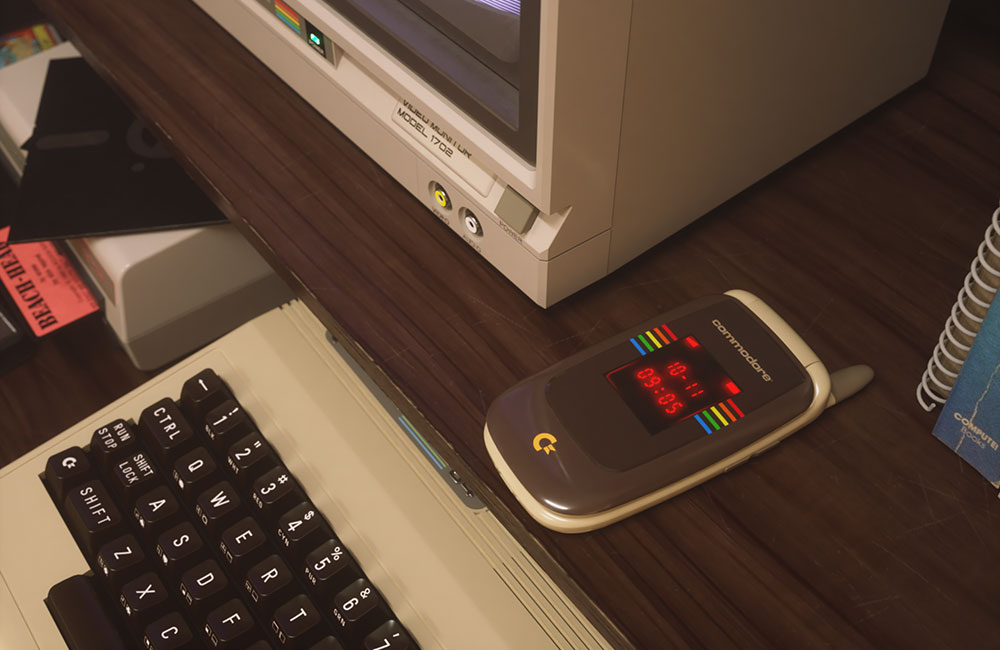 Commodore Callback flip phone beside a vintage Commodore computer and monitor.