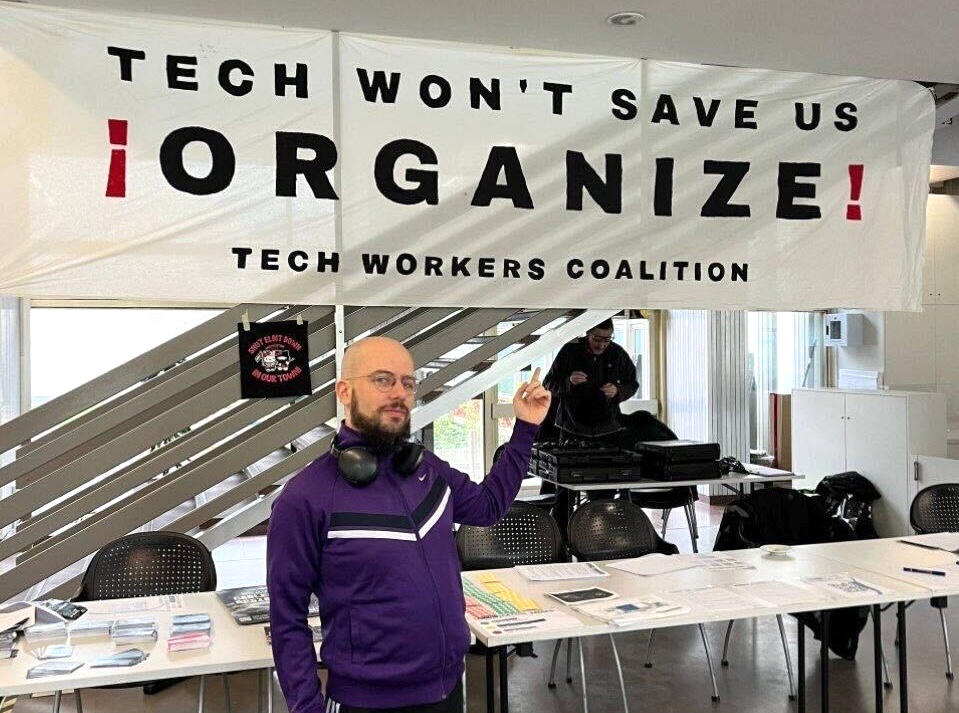 photo of simone robutti pointing to tech workers coalition sign that says tech won't save us - organize